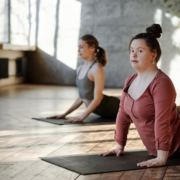 Two women practicing yoga indoors, emphasizing inclusivity and wellness.