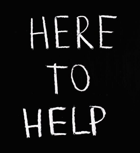 White text 'Here to Help' on a minimalist black chalkboard background, conveying encouragement and support.