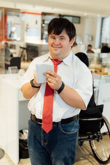 Confident man with Down syndrome smiling while holding a notepad in a modern office environment.