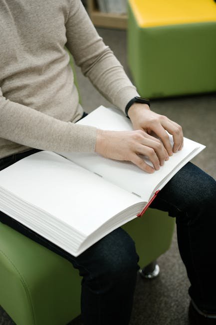 A person using fingers to read a braille book, sitting on a modern bench indoors.